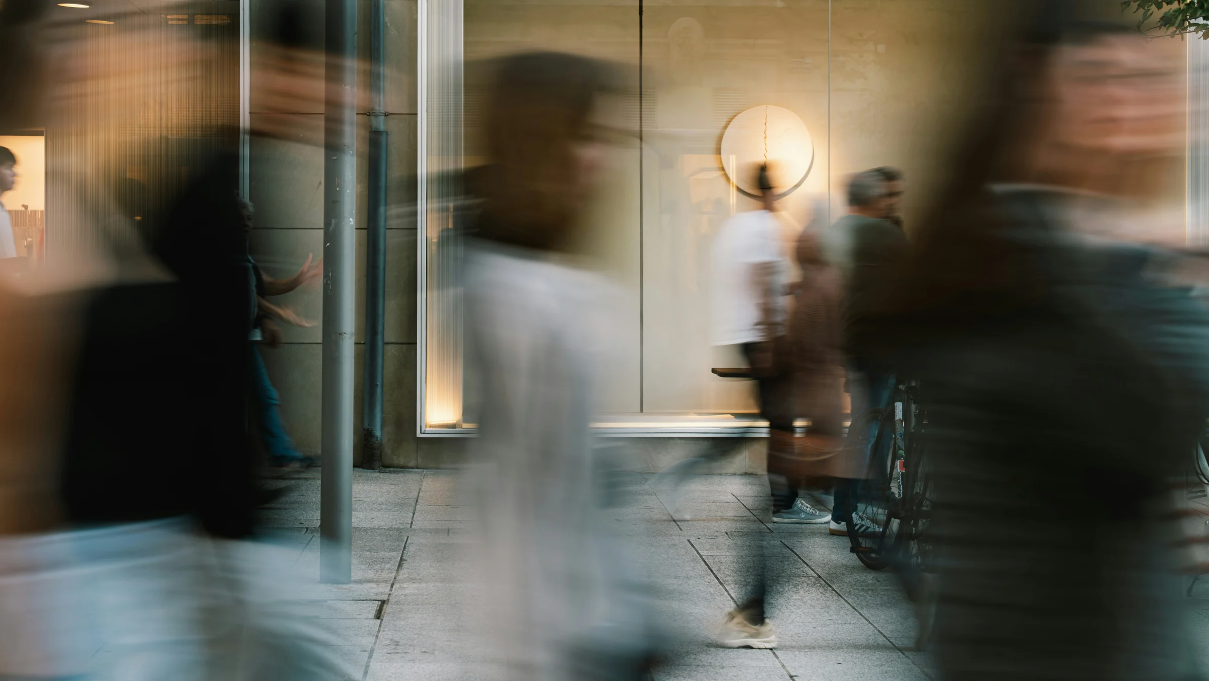People passing a warmly lit storefront, captured in motion.