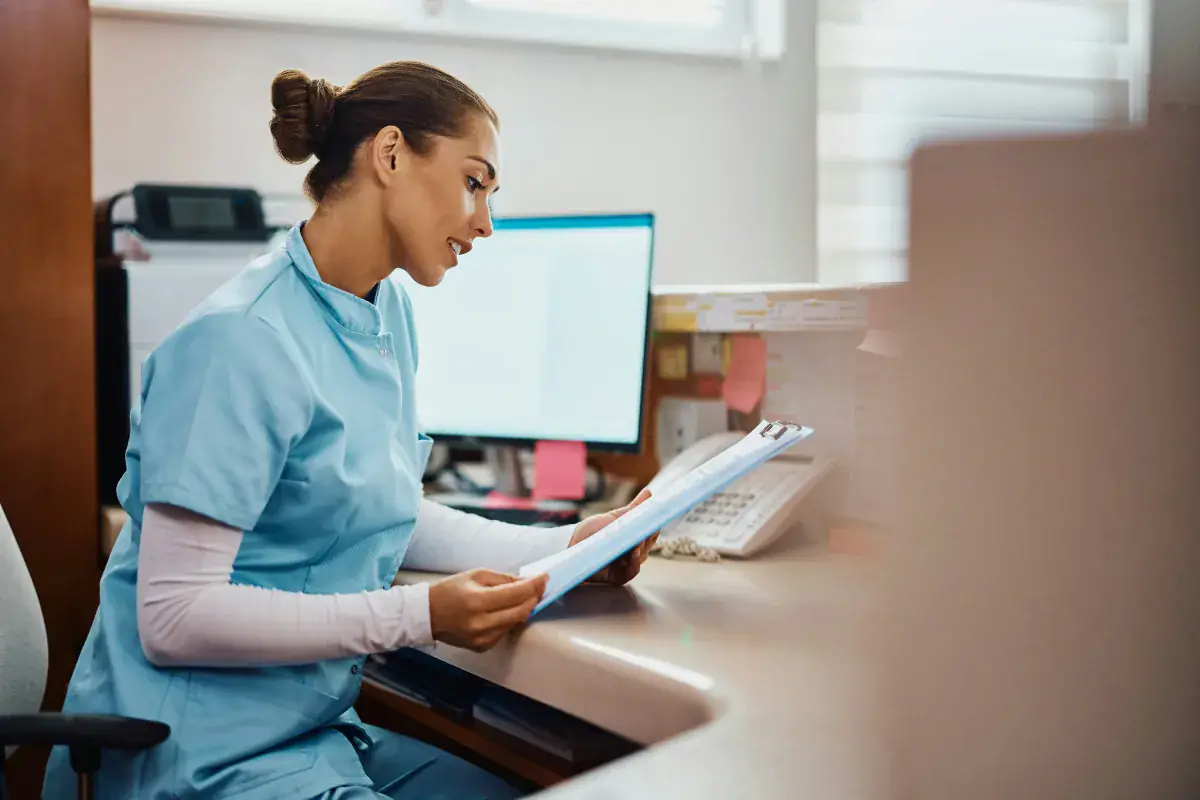 Healthcare staff member reviewing paperwork at a front desk