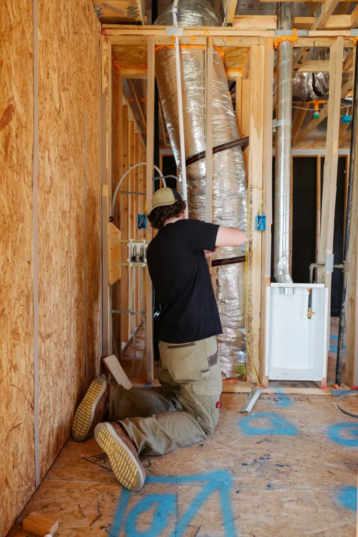 HVAC technician working on ductwork inside a wall frame